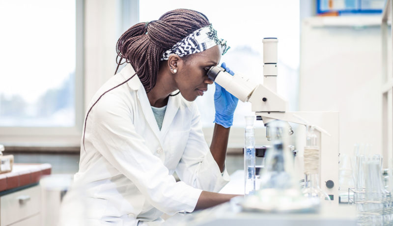 Female doctor studies biopsy under a microscope