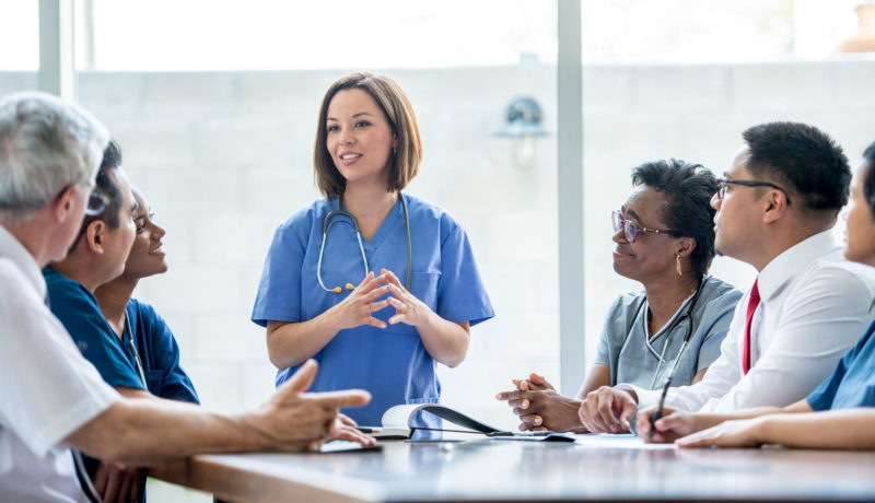 Young female doctor speaks to coworkers around a table