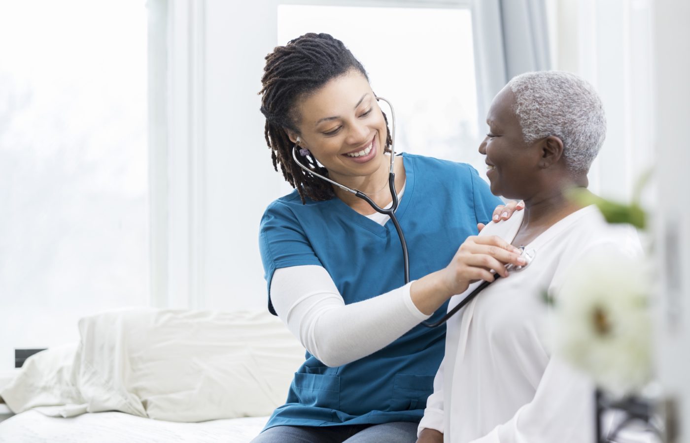 Young African American home healthcare nurse checks a senior female patient's vital signs. The senior woman is recovering at home from a recent surgery.