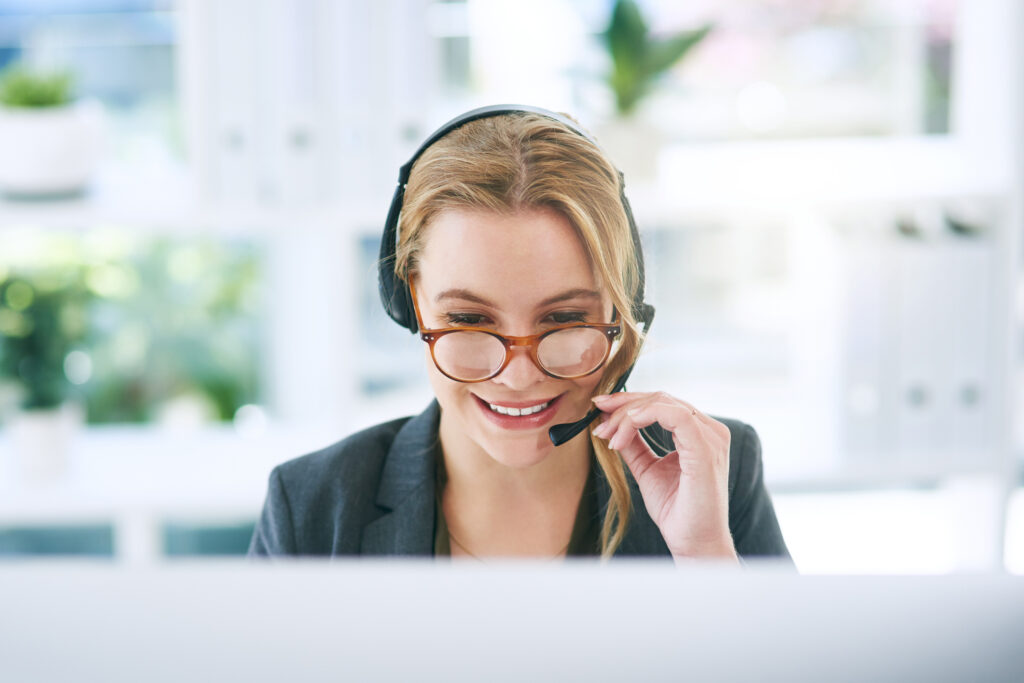 Shot of a confident young woman using a computer and headset in a modern office